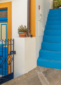Sicily - Sunny impressions of the Aeolian Islands, also known as Aeolian Islands or Isole Eolie: Lipari, Stromboli, Salina, Vulcano, Panarea, Filicudi and Alicudi. Steep blue concrete stairs next to a colorful front door on Panarea. Sicily - Sunny impressions of the Aeolian Islands, also known as Aeolian Islands or Isole Eolie: Lipari, Stromboli, Salina, Vulcano, Panarea, Filicudi and Alicudi. Steep blue concrete stairs next to a colorful front door on Panarea.
